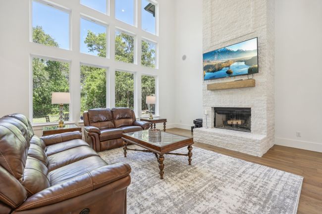 Living area with plenty of natural light, a towering ceiling, a stone fireplace, and wood finished floors | Image 9