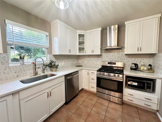 Kitchen with appliances with stainless steel finishes, wall chimney range hood, light tile patterned flooring, white cabinets, and backsplash | Image 6