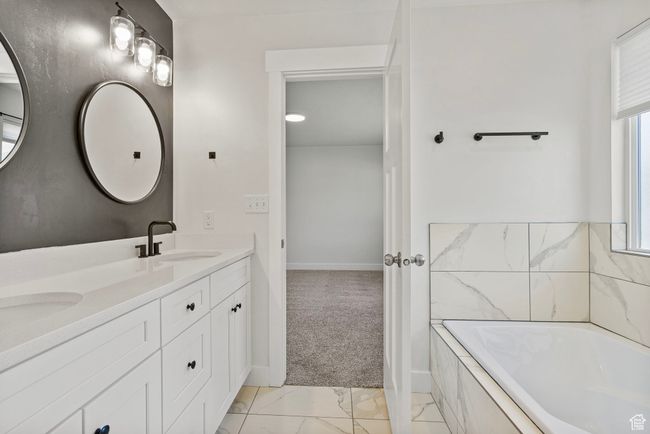 Full bath featuring marble look tiles, double vanity, healthy amount of natural light, and a bathtub | Image 14