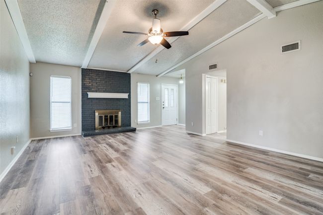 Unfurnished living room with a textured ceiling, ceiling fan, a brick fireplace, and wood finished floors | Image 4