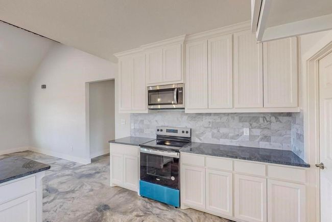 Kitchen featuring vaulted ceiling, white cabinets, stainless steel appliances, baseboards, and backsplash | Image 12