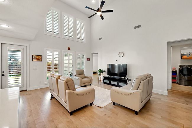 Living area with a ceiling fan, washer / dryer, light wood finished floors, a high ceiling, and baseboards | Image 7