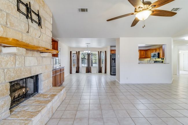 Unfurnished living room with light tile patterned floors, visible vents, ceiling fan with notable chandelier, and a stone fireplace | Image 9