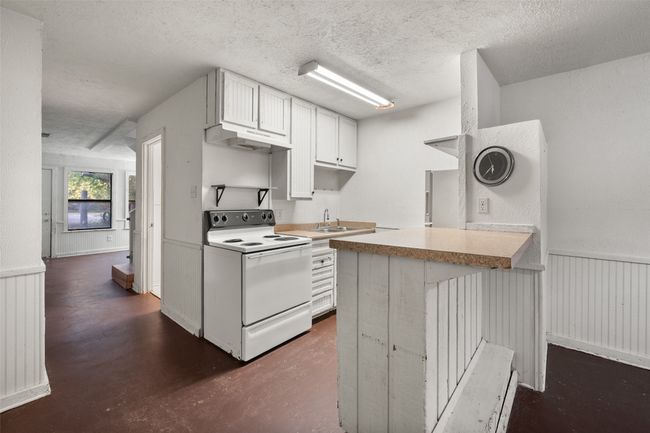 Kitchen featuring a wainscoted wall, light countertops, electric stove, a peninsula, and white cabinetry | Image 8