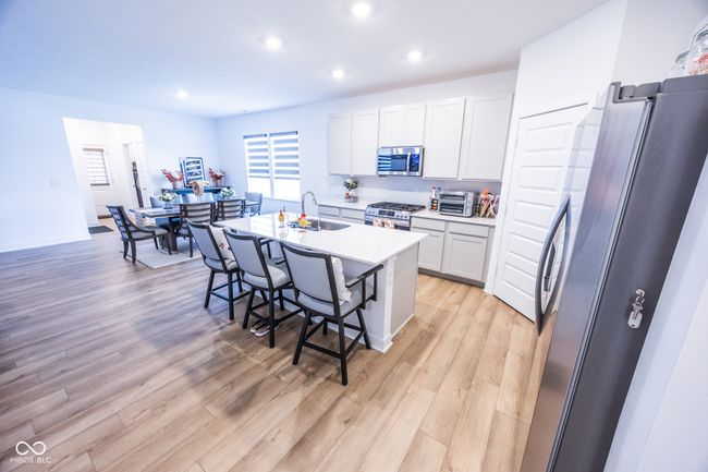 kitchen with appliances with stainless steel finishes, a sink, a kitchen breakfast bar, light wood-type flooring, and white cabinets | Image 8
