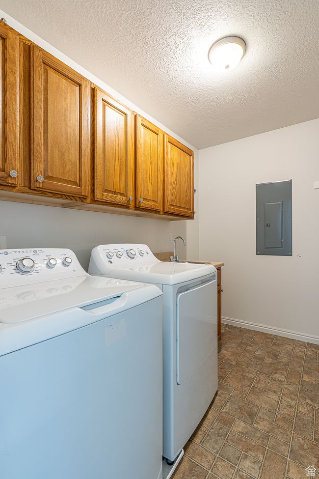 Laundry room featuring electric panel, washing machine and dryer, a textured ceiling, baseboards, and cabinet space | Image 25