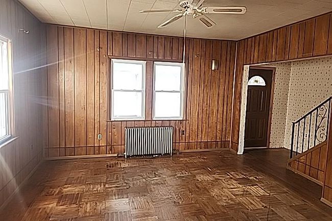 Unfurnished room with radiator heating unit, dark parquet floors, ceiling fan, and wood walls | Image 8