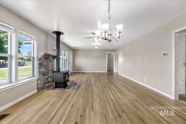 Unfurnished living room featuring a wood stove, wood finished floors, and a chandelier | Image 11