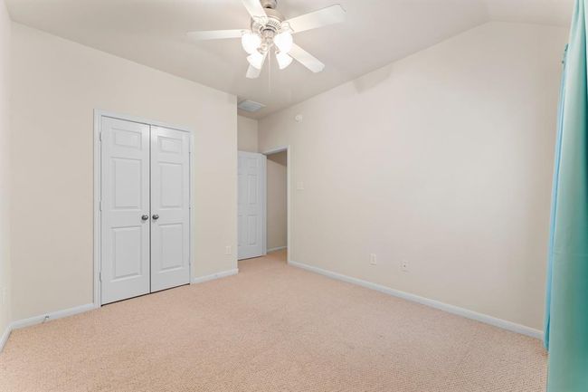 This light-filled secondary bedroom features a vaulted ceiling, neutral tones, double door closet and a large window overlooking the side yard. A ceiling fan and generous wall space make it a comfortable and versatile retreat for guests, children, or a home office. | Image 32
