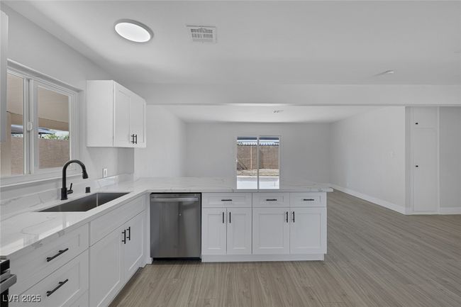 Kitchen featuring stainless steel dishwasher, a peninsula, white cabinetry, light wood finished floors, and light stone counters | Image 13