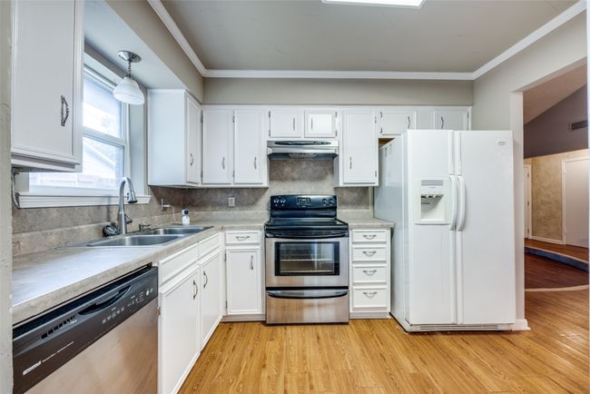 Kitchen with stainless steel appliances, under cabinet range hood, a sink, white cabinetry, and light wood finished floors | Image 9