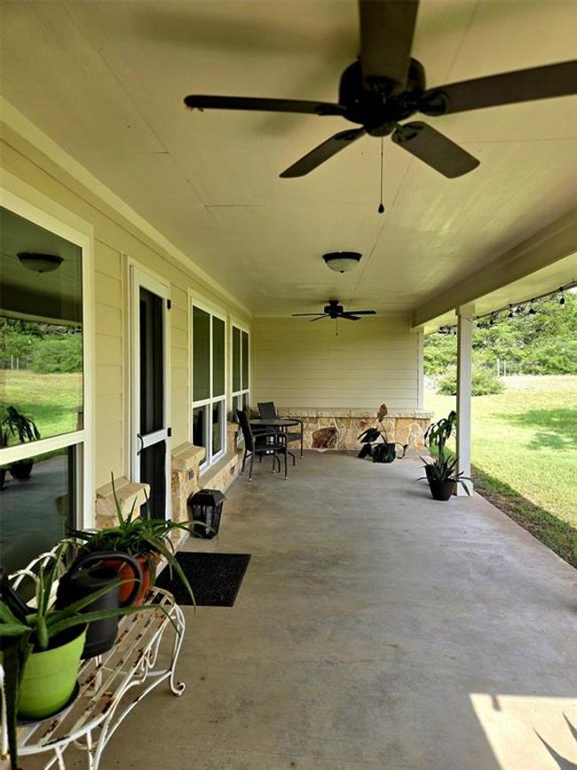 This photo showcases a spacious covered patio with ceiling fans, ample natural light from large windows, and a cozy seating area. It’s surrounded by lush greenery, offering a peaceful outdoor space for relaxation and entertainment. | Image 28