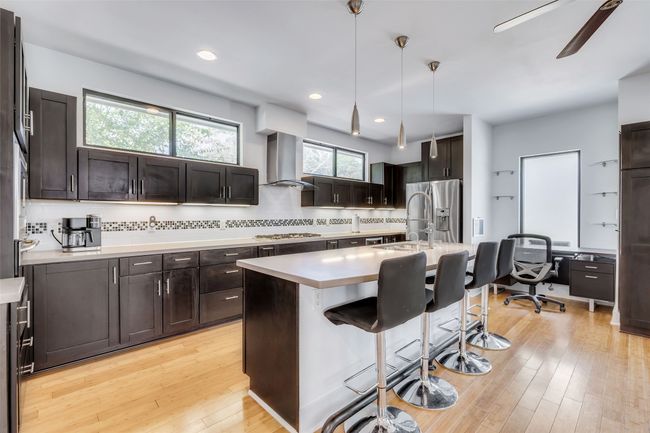 Kitchen featuring gas stovetop, extractor fan, stainless steel refrigerator with ice dispenser, decorative light fixtures, and a center island with sink | Image 8