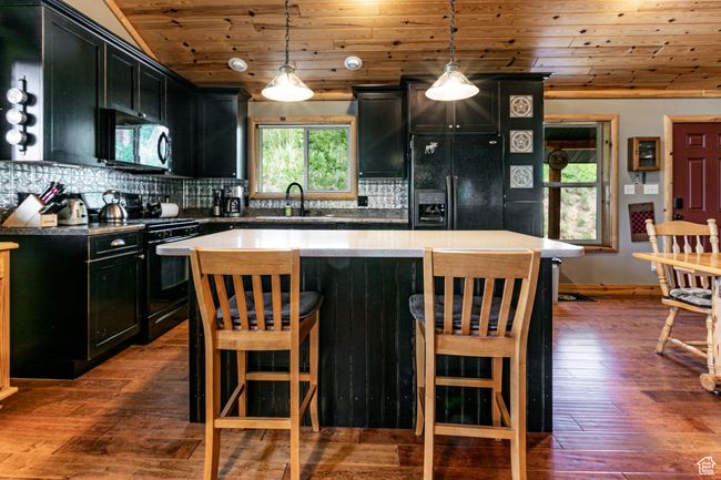 Kitchen with black appliances, dark cabinetry, wood ceiling, decorative backsplash, and dark wood finished floors | Image 12