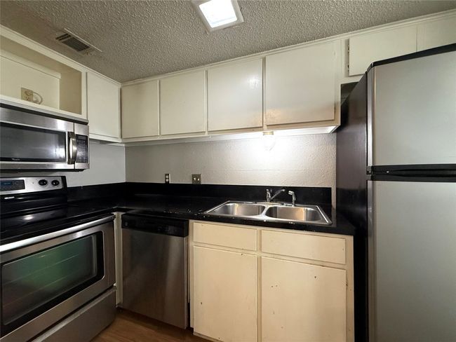 Kitchen with stainless steel appliances, a textured ceiling, open shelves, dark countertops, and white cabinetry | Image 7