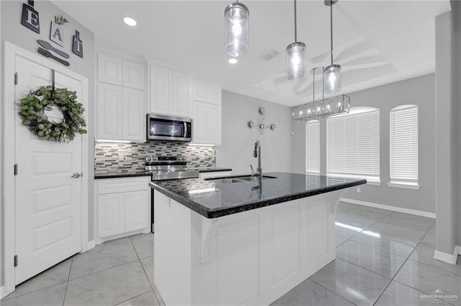 Kitchen with stainless steel microwave, light marble finish flooring, backsplash, and white cabinetry | Image 11