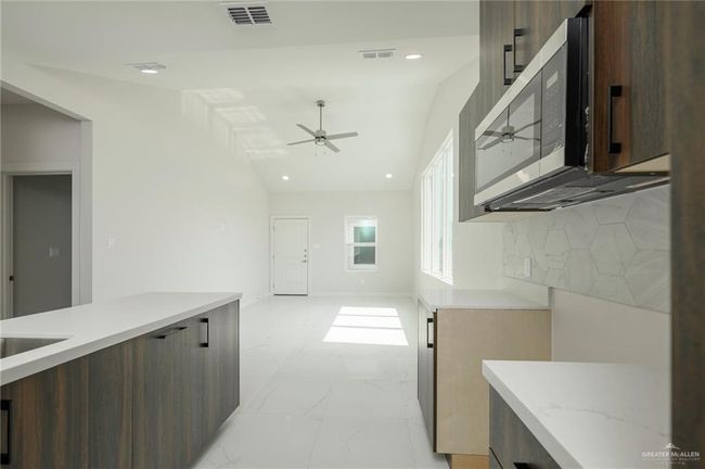 Kitchen with modern cabinets, stainless steel microwave, a ceiling fan, light marble finish floors, and lofted ceiling | Image 11