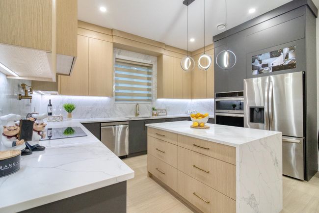 Kitchen with light brown cabinetry, appliances with stainless steel finishes, modern cabinets, a sink, and light stone countertops | Image 9