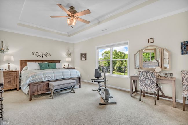 primary bedroom featuring a tray ceiling, crown molding, carpet, ceiling fan, and walk-in closet | Image 33