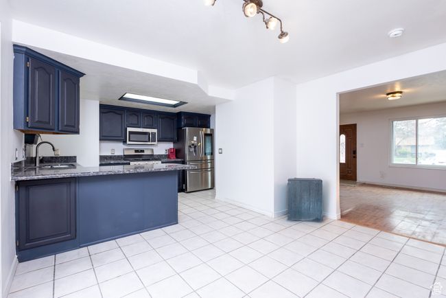 Kitchen with dark stone countertops, a sink, a peninsula, stainless steel appliances, and blue cabinetry | Image 7