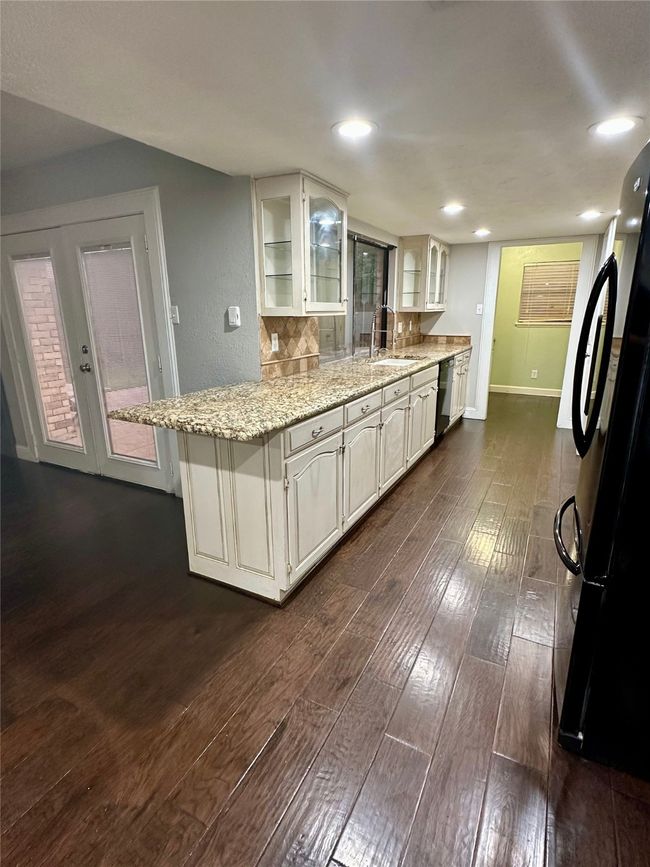 Kitchen featuring dark wood-style floors, glass insert cabinets, freestanding refrigerator, light stone counters, and white cabinets | Image 12