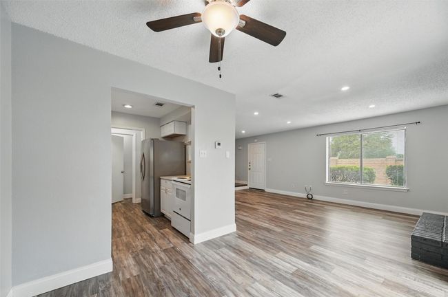 Unfurnished living room with a textured ceiling, wood finished floors, recessed lighting, and a ceiling fan | Image 6