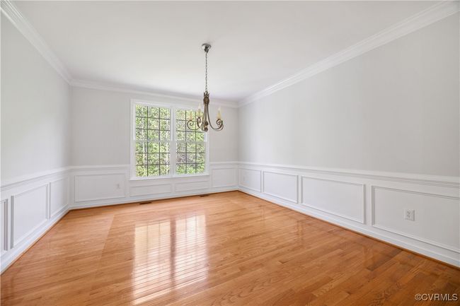 Empty room featuring ornamental molding, a wainscoted wall, light wood-style flooring, and a chandelier | Image 12