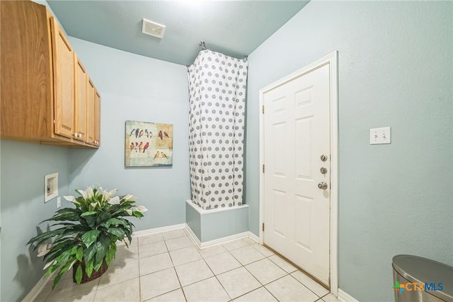 Large Laundry Room with cabinet storage. The water heater is tucked behind the curtain. The door to the garage is pictured. | Image 15