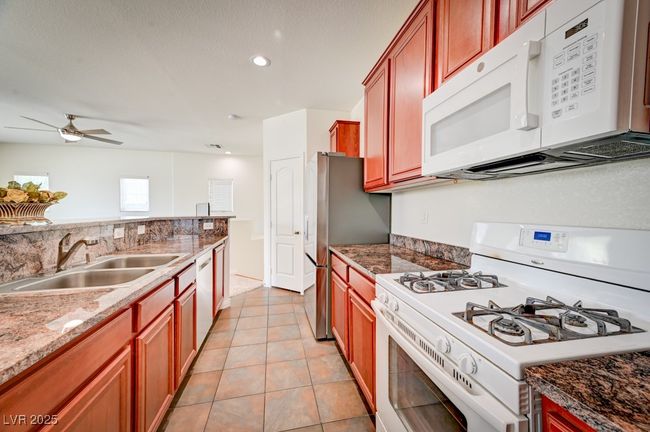 Kitchen with white appliances, a ceiling fan, light tile patterned floors, recessed lighting, and stone countertops | Image 12