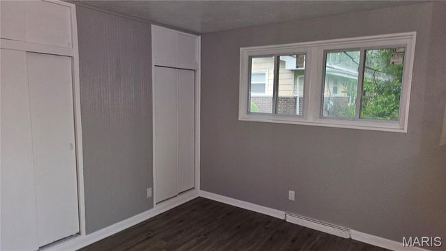 Unfurnished bedroom featuring dark wood finished floors and a baseboard heating unit | Image 11