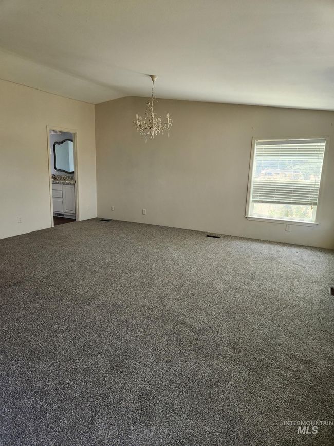 Carpeted empty room featuring a chandelier and vaulted ceiling | Image 8