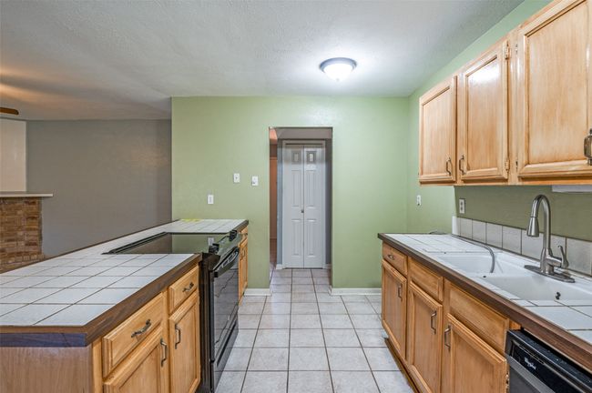 Kitchen with black appliances, tile countertops, light tile patterned flooring, and a textured ceiling | Image 6