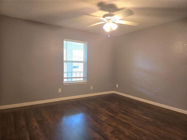 This room features freshly painted gray walls, rich wood flooring, a window providing natural light, and a ceiling fan, creating a modern and comfortable space. | Image 9