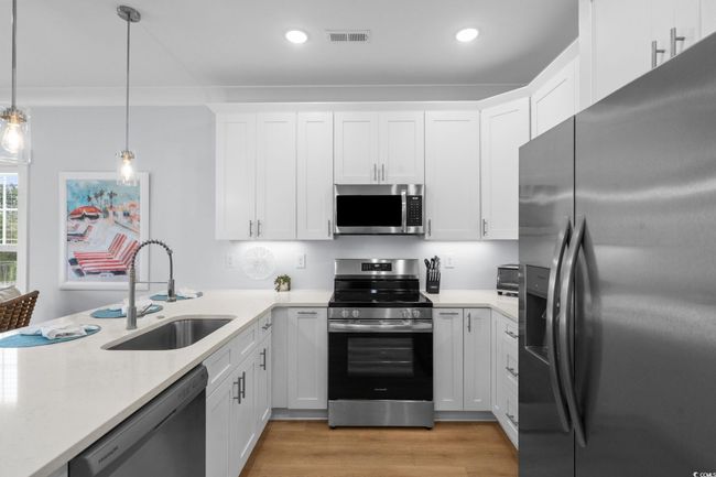 Kitchen featuring appliances with stainless steel finishes, white cabinetry, hanging light fixtures, light wood-style floors, and light stone counters | Image 10