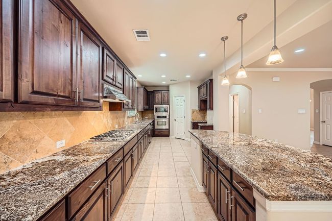 Kitchen featuring appliances with stainless steel finishes, arched walkways, under cabinet range hood, tasteful backsplash, and stone counters | Image 9