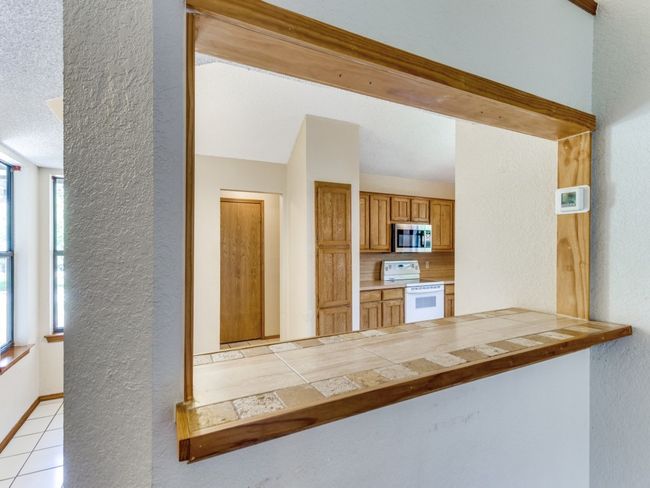 Kitchen with white electric range, stainless steel microwave, a textured wall, tasteful backsplash, and tile counters | Image 24
