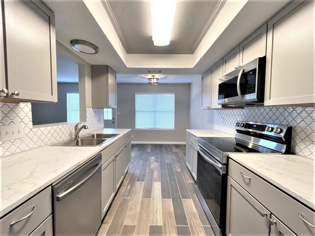 Kitchen with stainless steel appliances, a tray ceiling, a sink, wood finished floors, and baseboards | Image 7