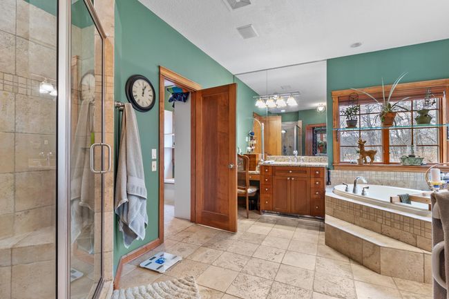 Primary bath with custom tile flooring and custom tile shower. Large tub with jets. Two separate sink areas and dressing table. Entry to second primary walk-in closet shown. | Image 25