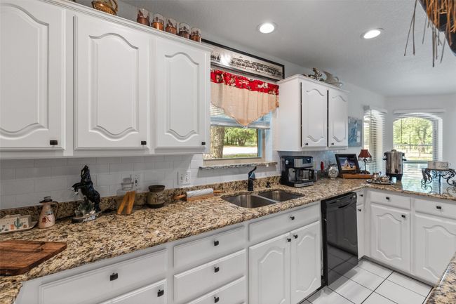 Kitchen with light tile patterned floors, white cabinets, black dishwasher, a sink, and backsplash | Image 9