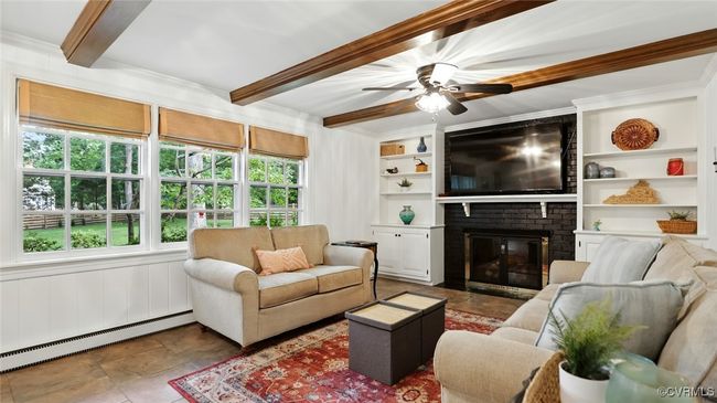 Living room with a baseboard heating unit, beamed ceiling, a brick fireplace, a ceiling fan, and ornamental molding | Image 32