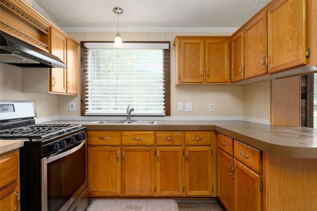 Kitchen featuring stainless steel gas stove, a sink, a textured ceiling, crown molding, and wall chimney exhaust hood | Image 25