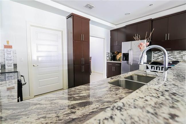 Kitchen with light stone counters, visible vents, backsplash, a sink, and stainless steel fridge | Image 7