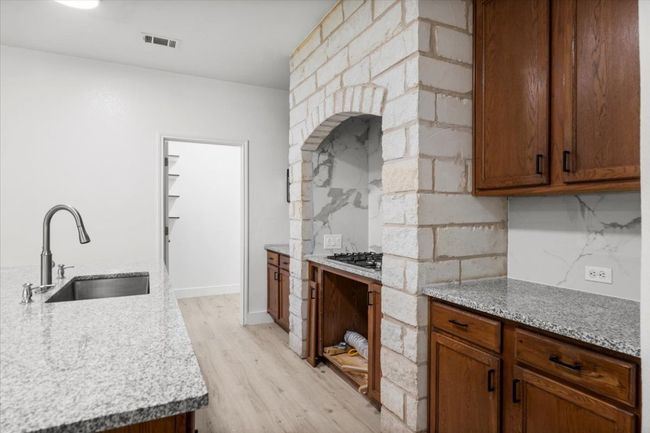 Kitchen with light wood-style floors, backsplash, brown cabinetry, and stainless steel gas stovetop | Image 11