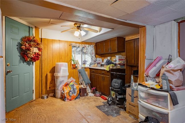 Kitchen featuring ceiling fan, wooden walls, brown cabinetry, and light countertops | Image 9