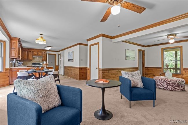 Living area featuring a wainscoted wall, wooden walls, ceiling fan, light colored carpet, and ornamental molding | Image 4