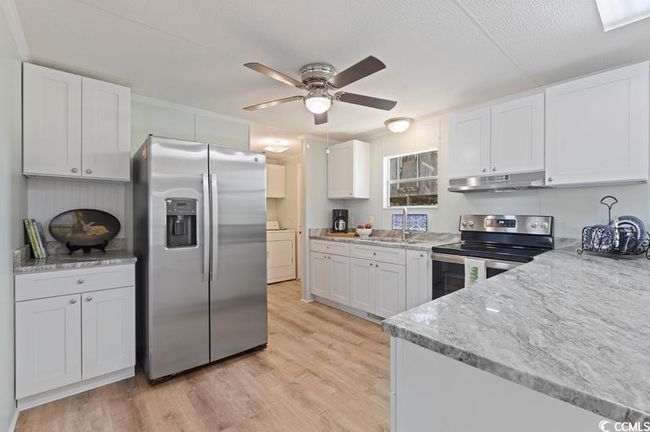 Kitchen with appliances with stainless steel finishes, under cabinet range hood, washer / clothes dryer, ceiling fan, and white cabinetry | Image 17