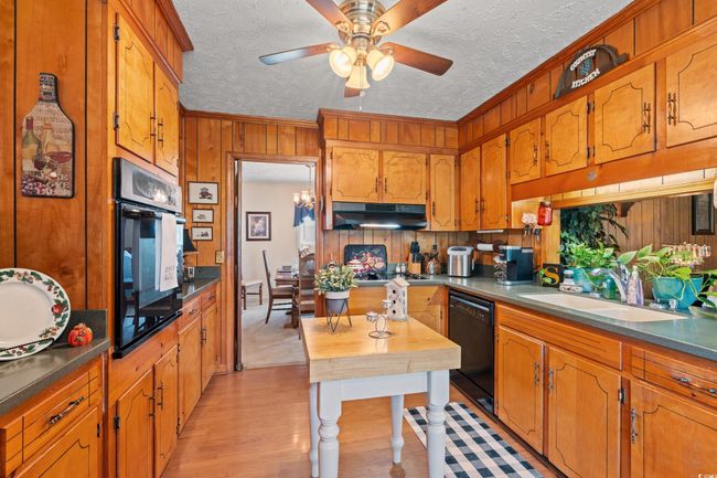 Kitchen with a sink, black appliances, wooden walls, ceiling fan, and under cabinet range hood | Image 5