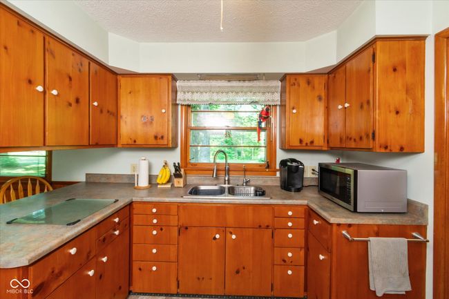 kitchen featuring stainless steel microwave, black electric cooktop, a textured ceiling, and brown cabinetry | Image 13