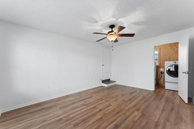 This room features fresh white walls, wood-style flooring, and a ceiling fan for comfort. It includes convenient access to a laundry area with a washer and dryer. | Image 28