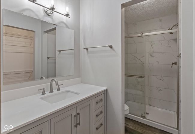 full bath featuring a shower stall, a textured ceiling, vanity, wood finished floors, and a spacious closet | Image 14